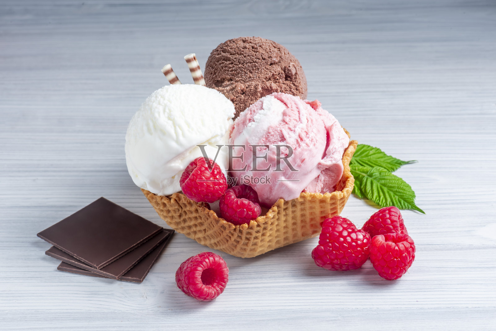 三勺冰淇淋:白色的、棕色的和粉色的，装在一个华夫玻璃杯里，放在木桌上。照片摄影图片