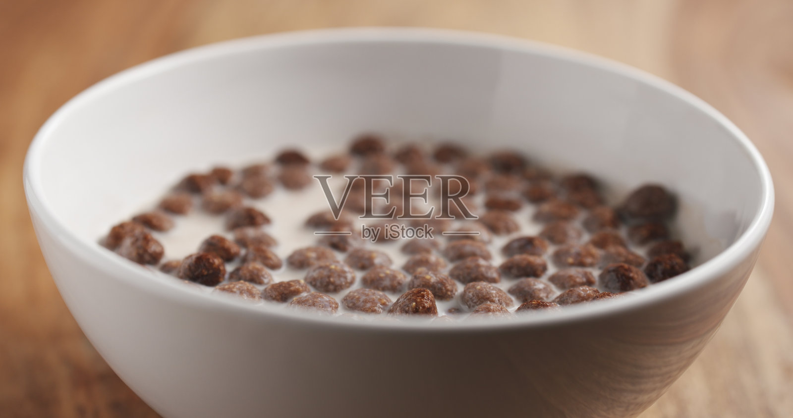 木桌上白色碗里的谷物巧克力球和牛奶的特写照片摄影图片