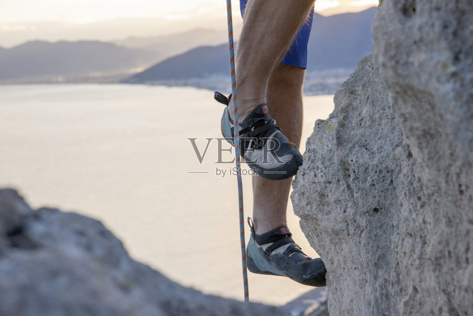 攀爬海上陡峭悬崖的攀岩者的腿照片摄影图片