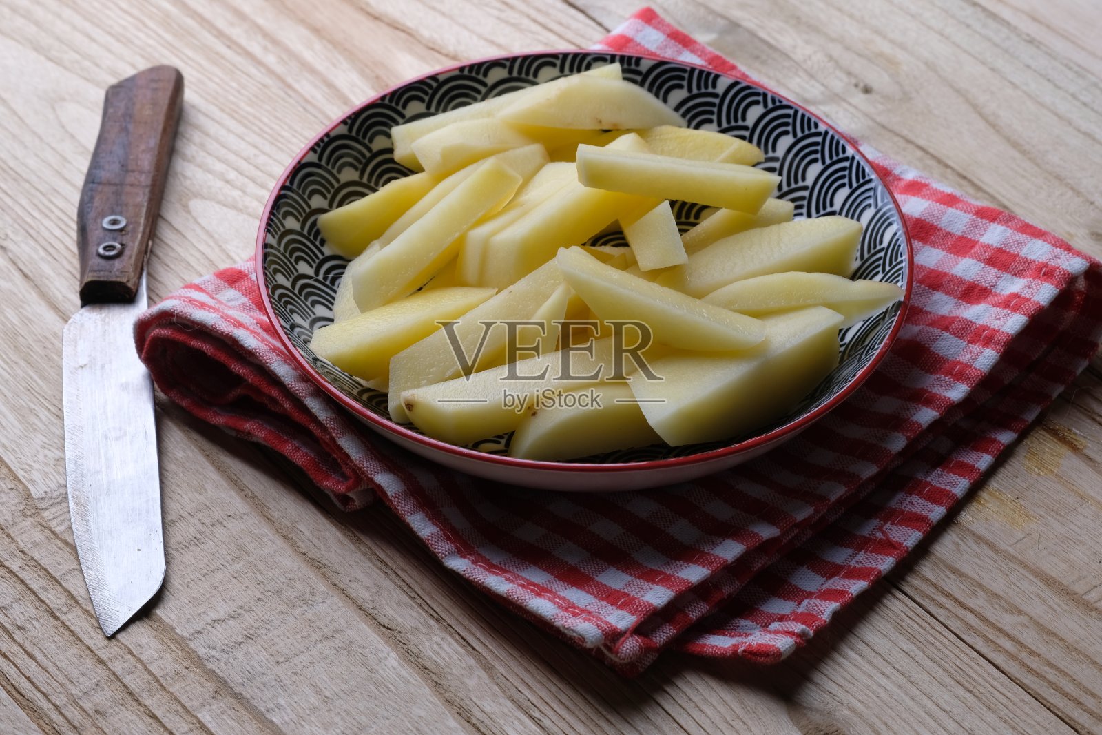 陶瓷盘子里的生薯条。生土豆片。碳水化合物。主食。健唐iris mentah。盘子旁边放着一把刀。照片摄影图片