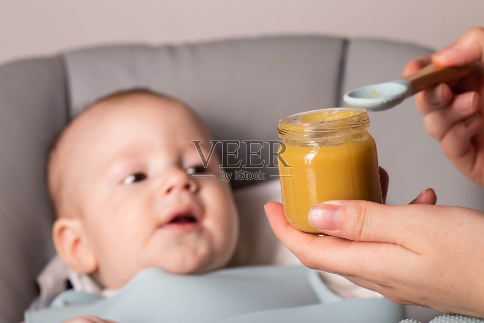 母亲拿着一罐蔬菜泥，背景是一个6个月大的婴儿。婴儿的第一种食物，特写照片摄影图片