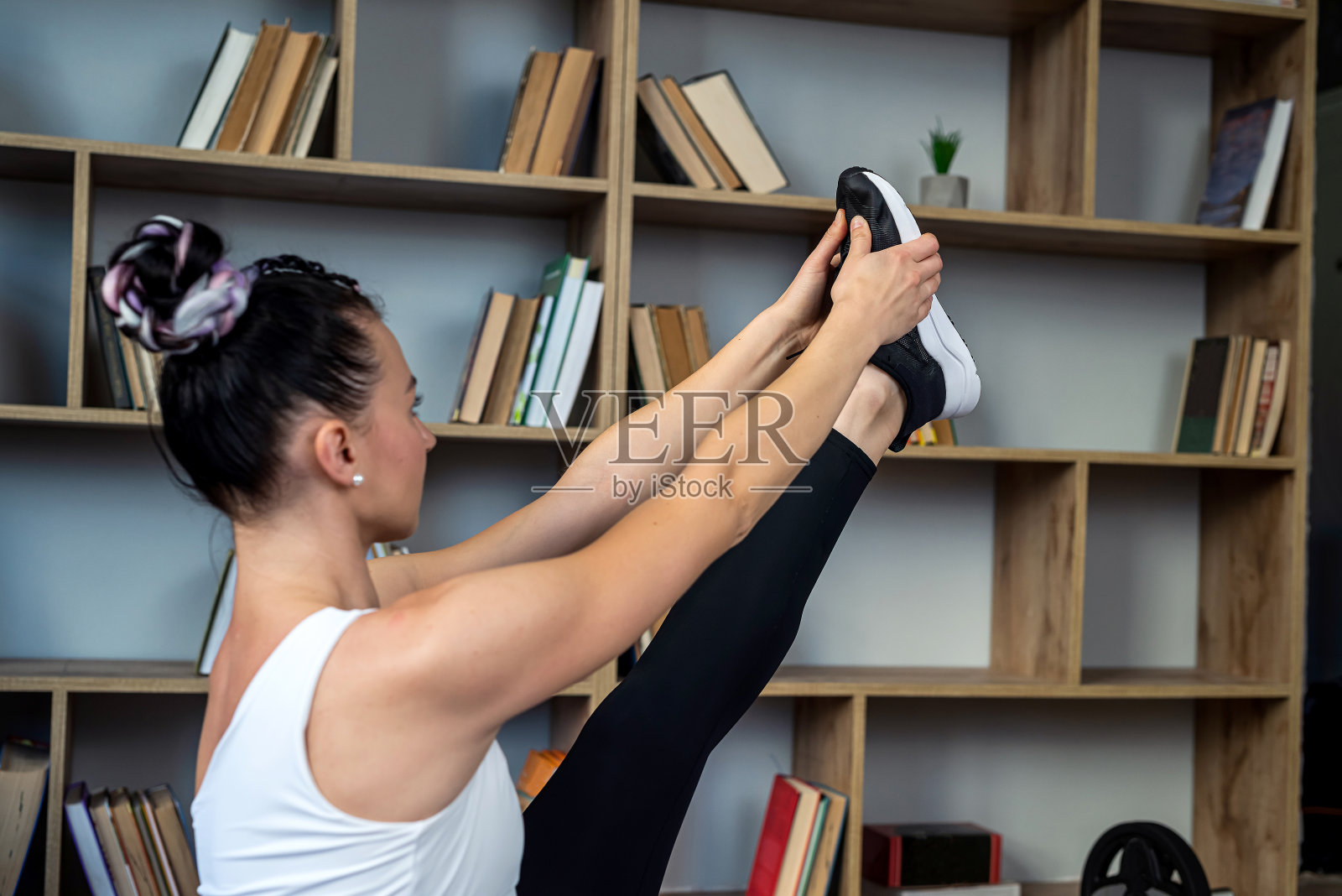 穿着运动服的女子坐在图书馆大厅的垫子上做瑜伽姿势。照片摄影图片