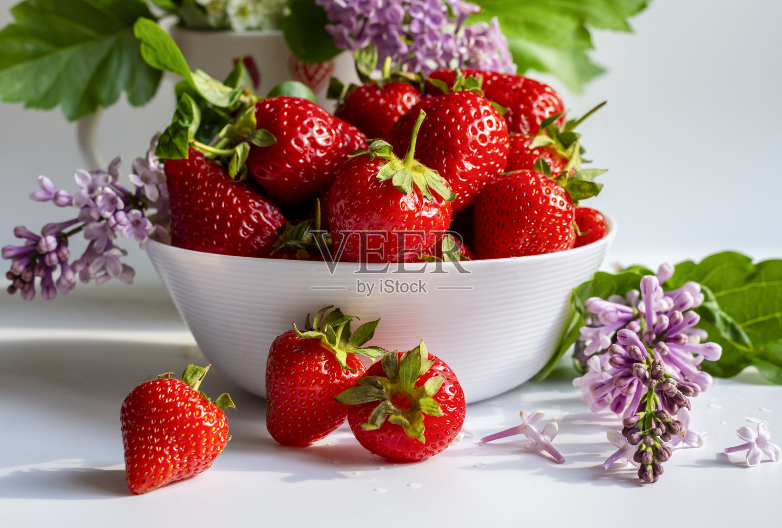 成熟多汁的草莓在一个白色的杯子和丁香花照片摄影图片