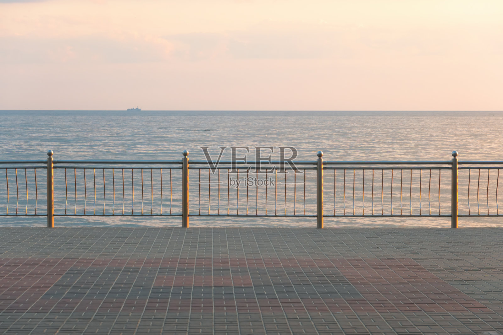 清晨的海景。河堤上有一道金属栅栏，地平线上有一艘船的剪影。初升的太阳照亮了风景。照片摄影图片