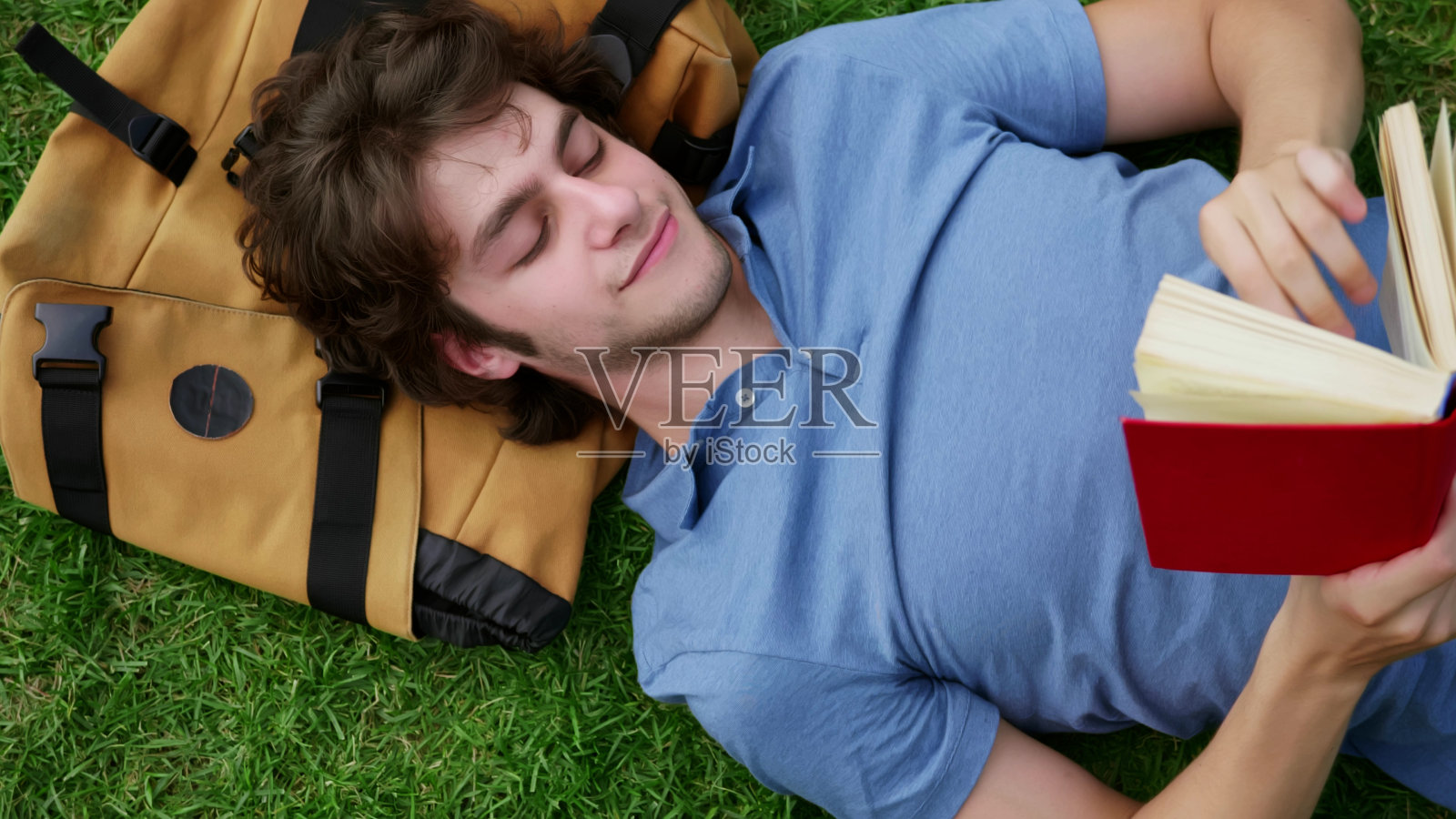 俯视图，年轻人躺在草地上看书，头靠在背包上照片摄影图片