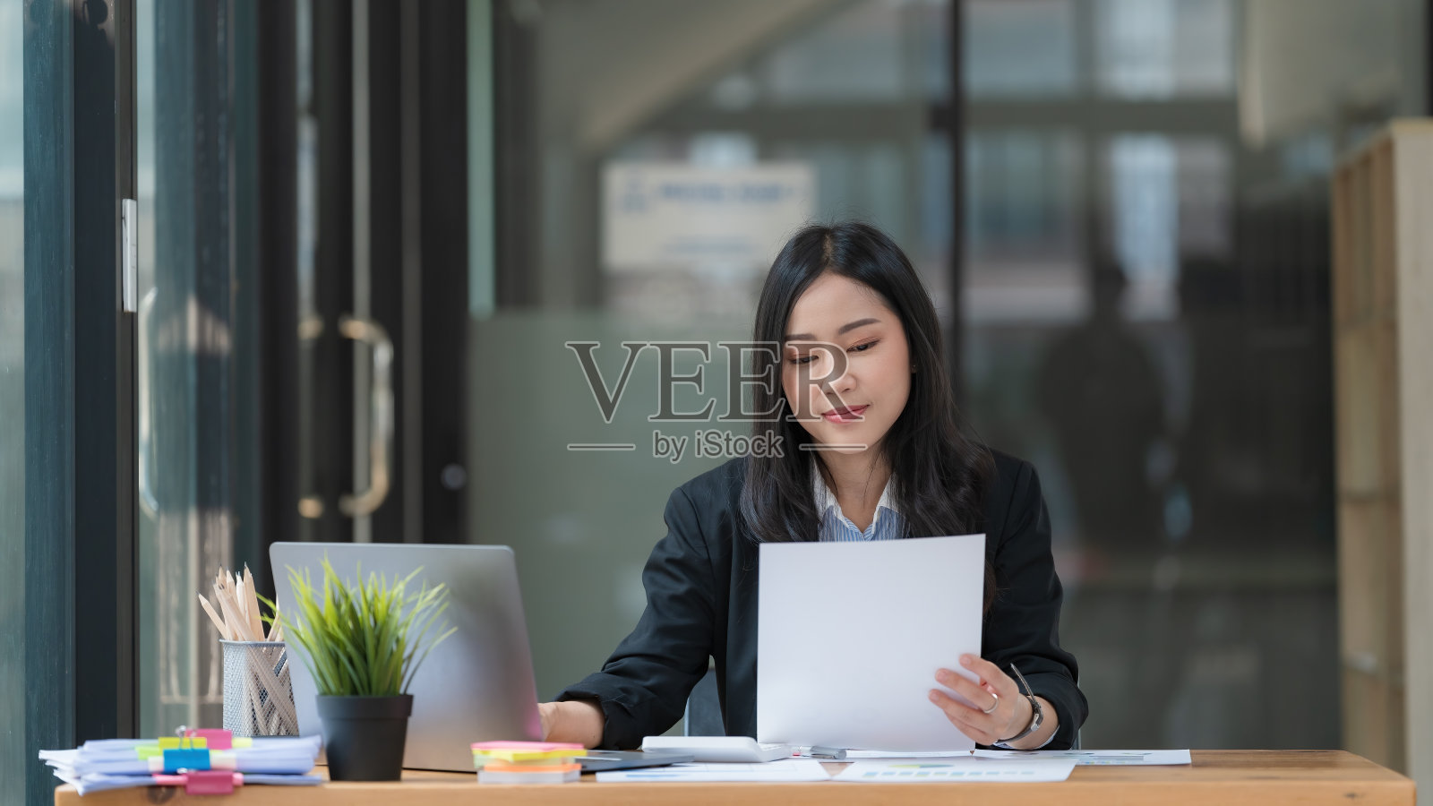 一位亚洲女商人在她的办公桌前用笔记本电脑工作。照片摄影图片