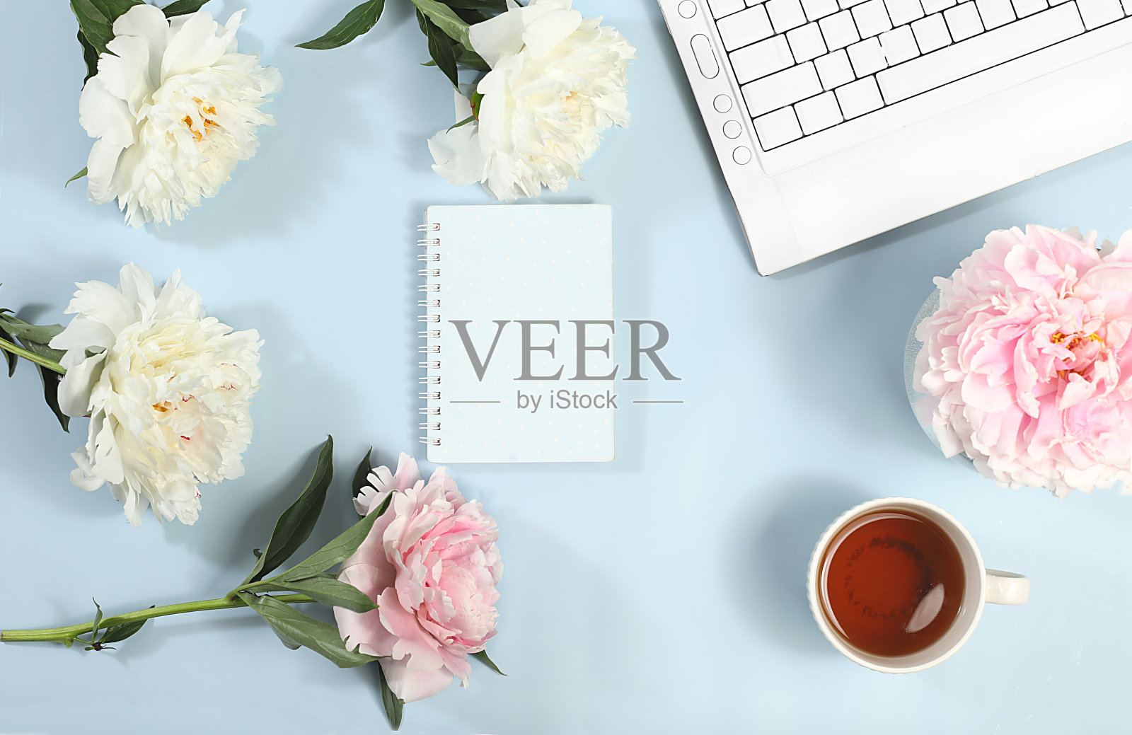 电脑，牡丹花和一杯咖啡放在一张浅色的桌子上。现代女性的桌面，家庭办公室。最小经营理念照片摄影图片