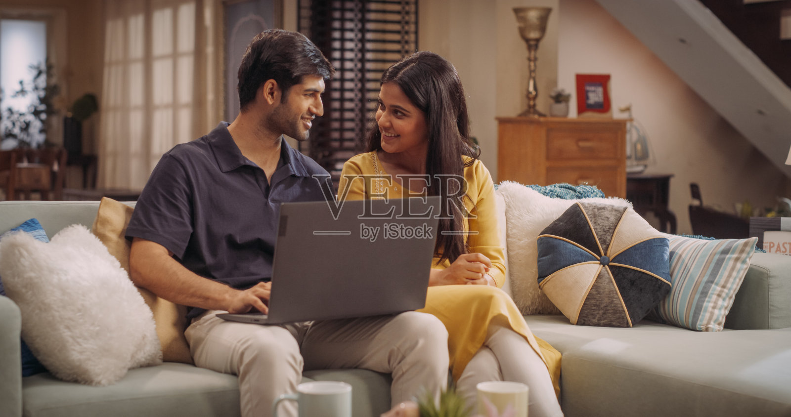 一对可爱的印度年轻夫妇喜欢坐在客厅的沙发上，一起用笔记本电脑浏览网上购物网站。浏览网页，选择购买的产品照片摄影图片