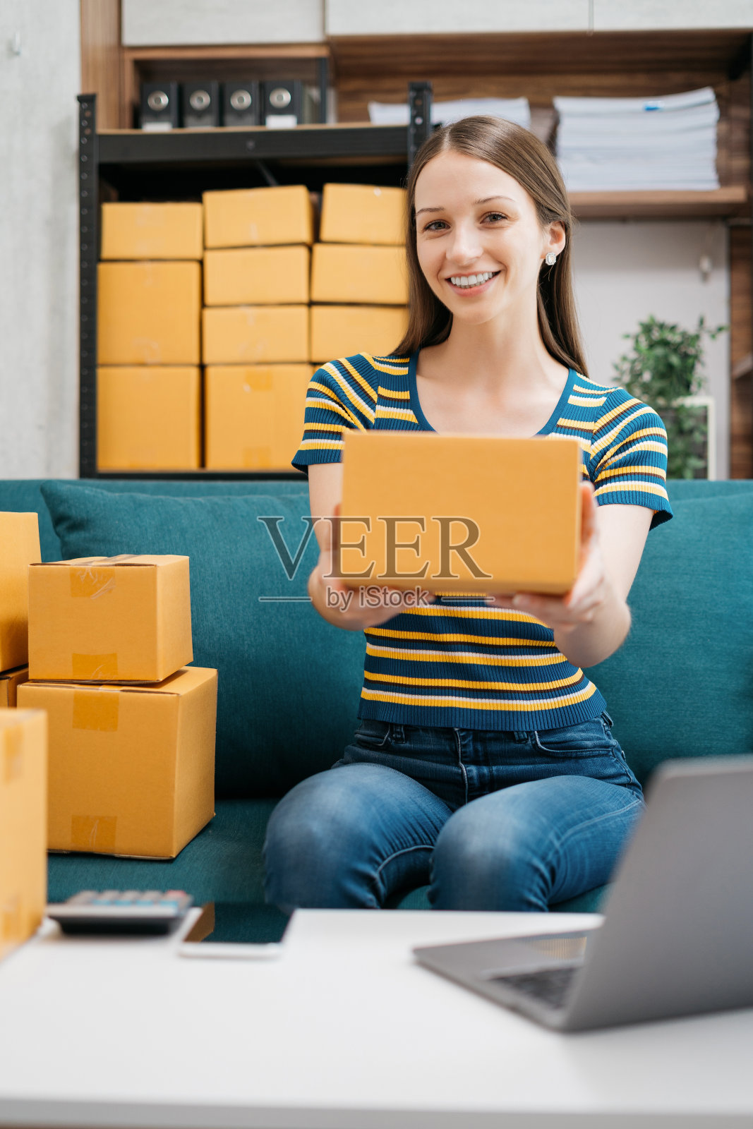 一名女子拿着包裹，看着镜头，站在家里办公室的几个盒子中间。照片摄影图片