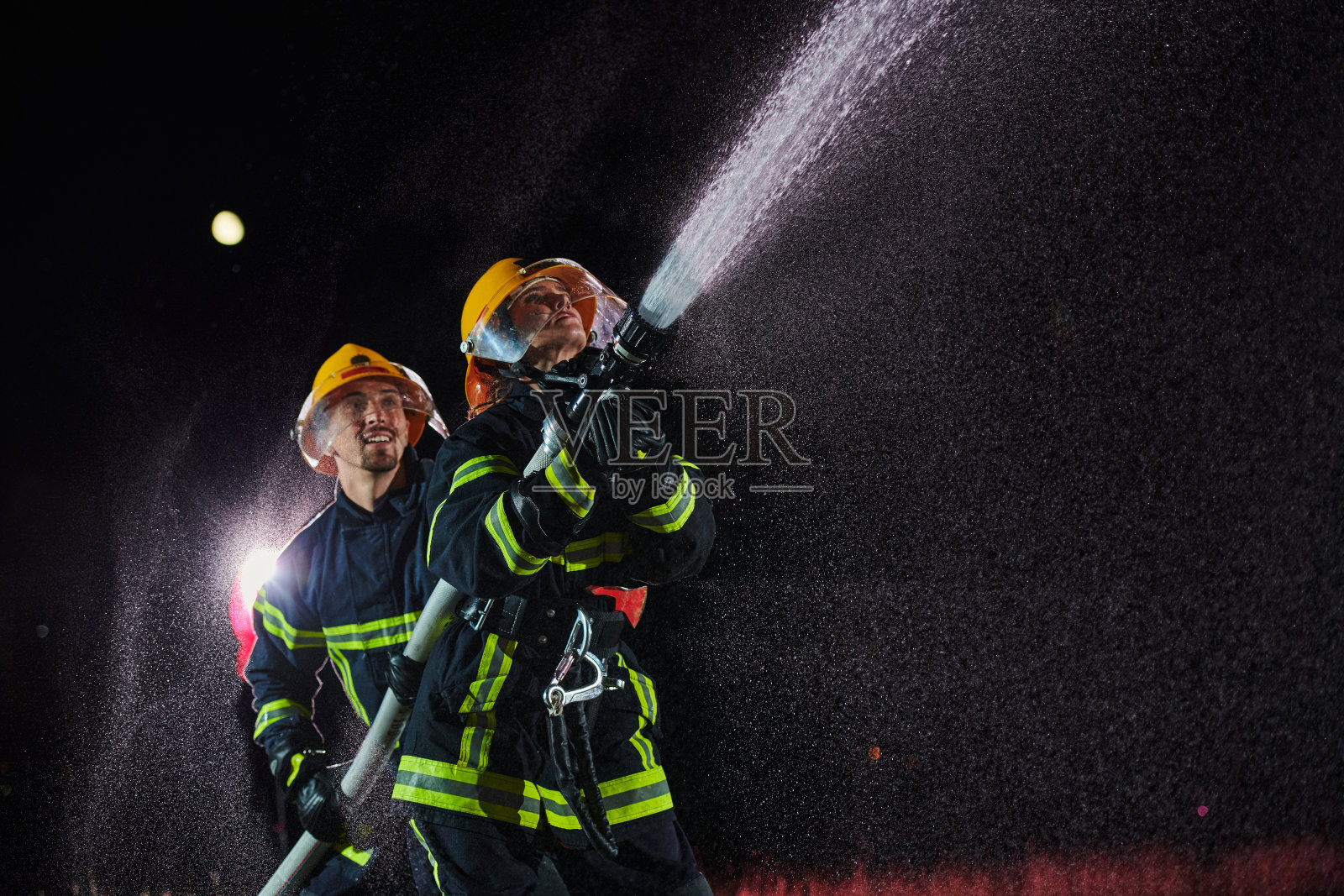 消防队员使用水管消除火灾隐患。一队男女消防员在危险的救援任务。照片摄影图片