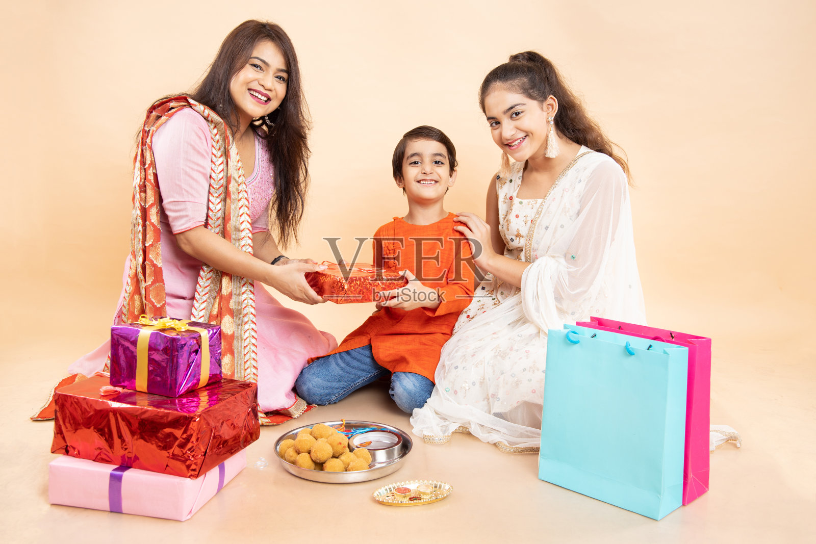 年轻的印度孩子兄弟姐妹庆祝rakshabandhan或bhai dooj节，大礼盒，购物袋和盘子里的甜laddoo，孤立的背景。照片摄影图片