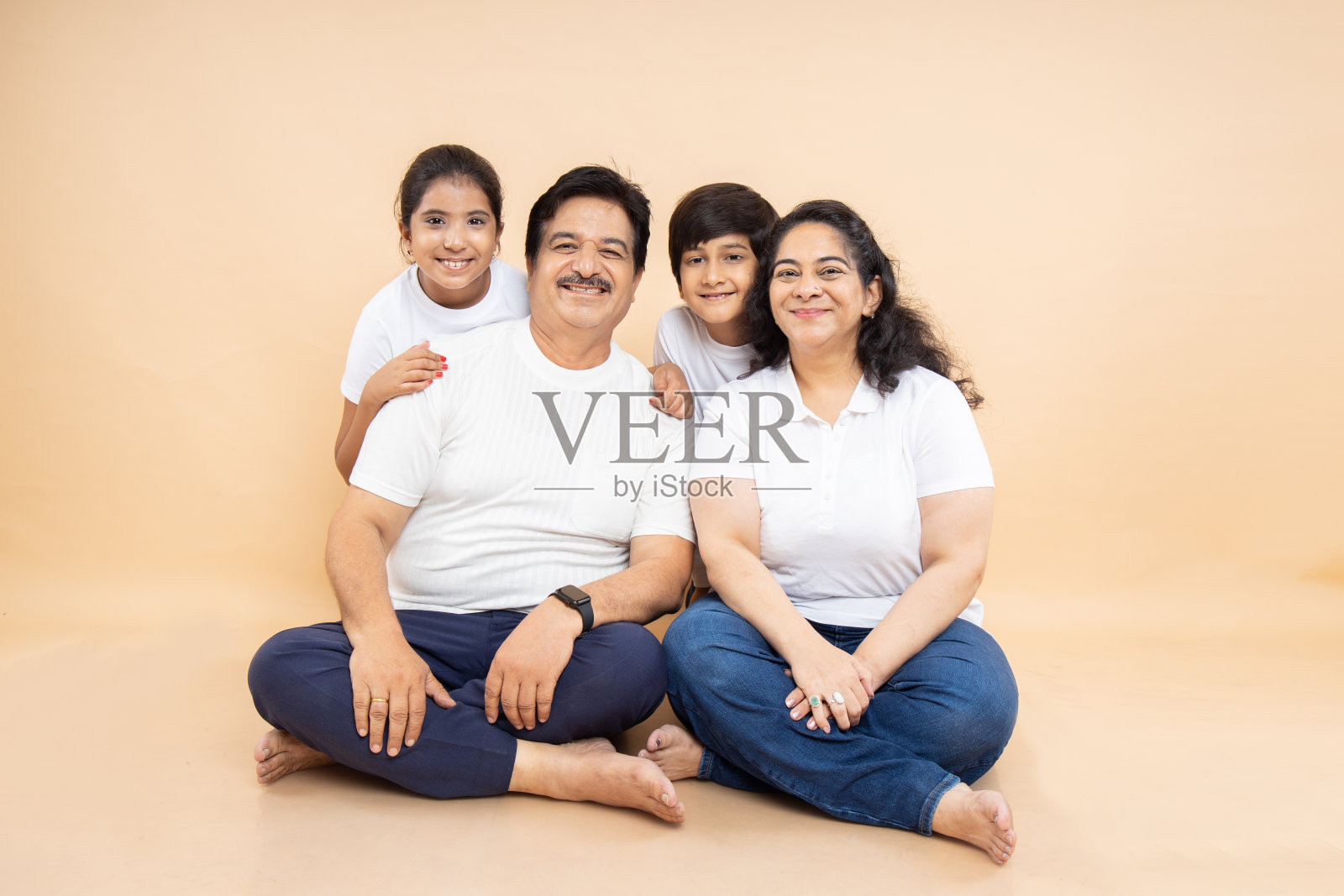 快乐的印度祖父母和孩子们穿着白色休闲t恤坐在一起，在米色的背景下孤立地坐着。照片摄影图片