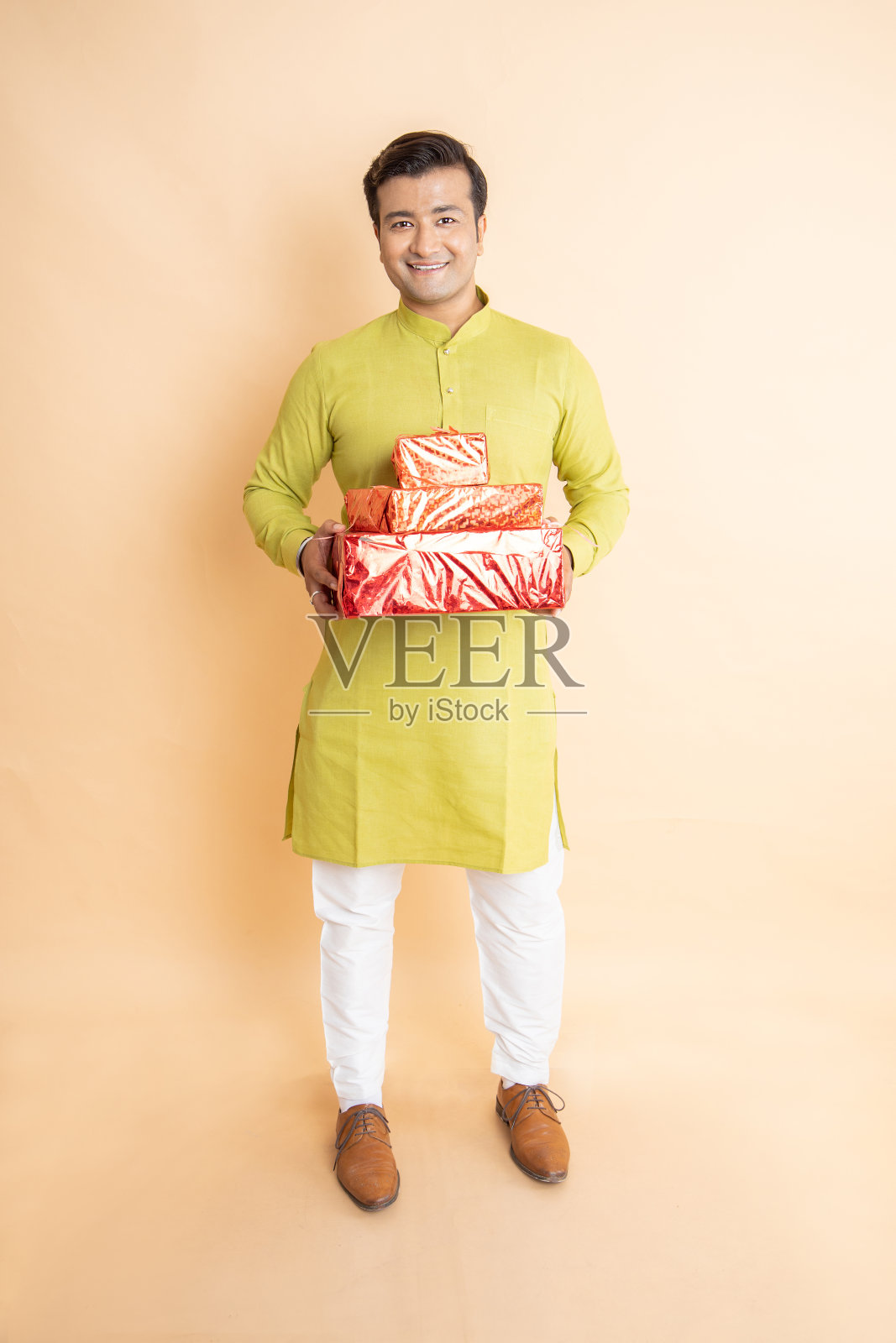 快乐英俊的印度男人穿着传统的kurta服装，拿着红色的礼盒庆祝排灯节，独自在工作室背景。照片摄影图片