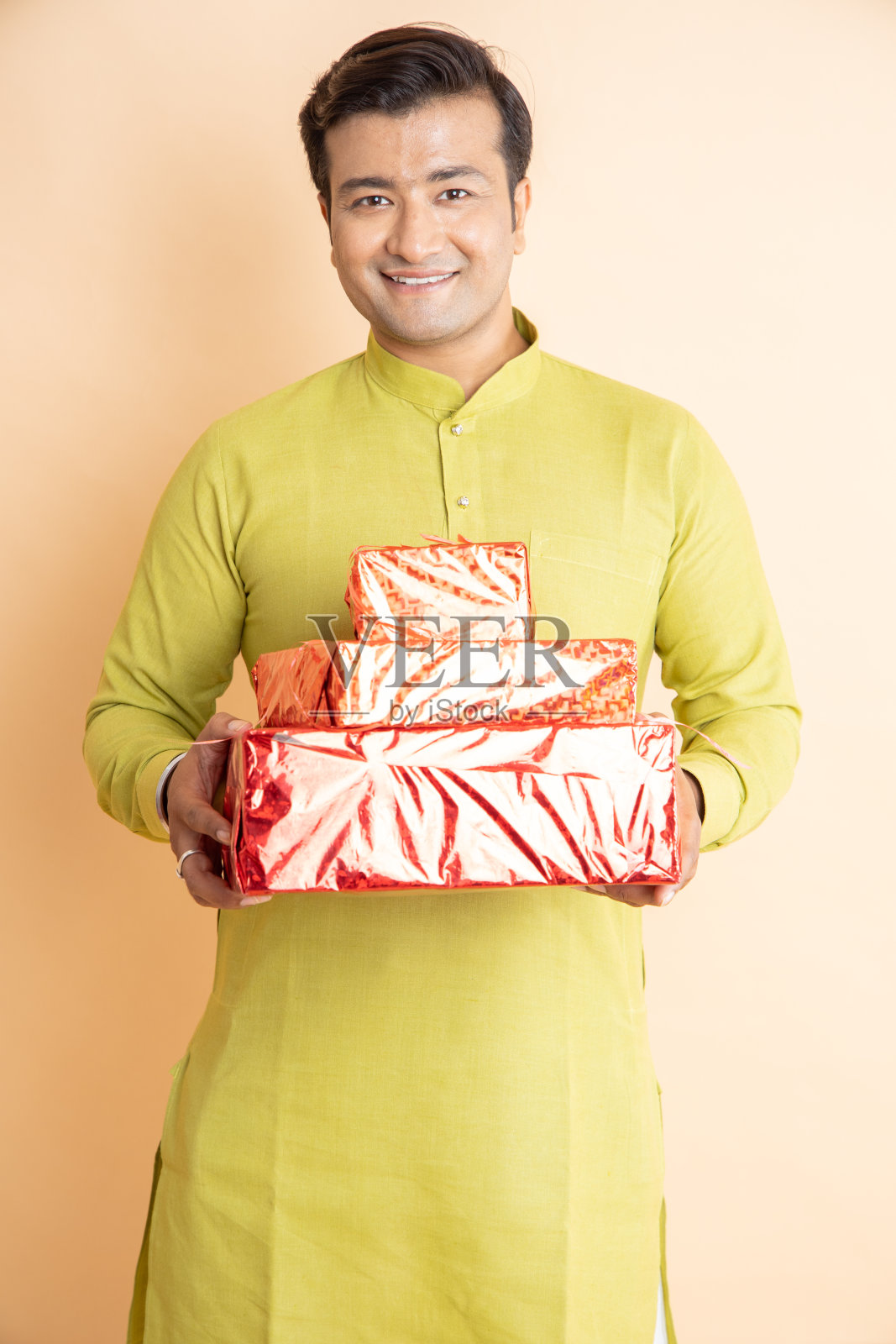 快乐英俊的印度男人穿着传统的kurta服装，拿着红色的礼盒庆祝排灯节，独自在工作室背景。照片摄影图片