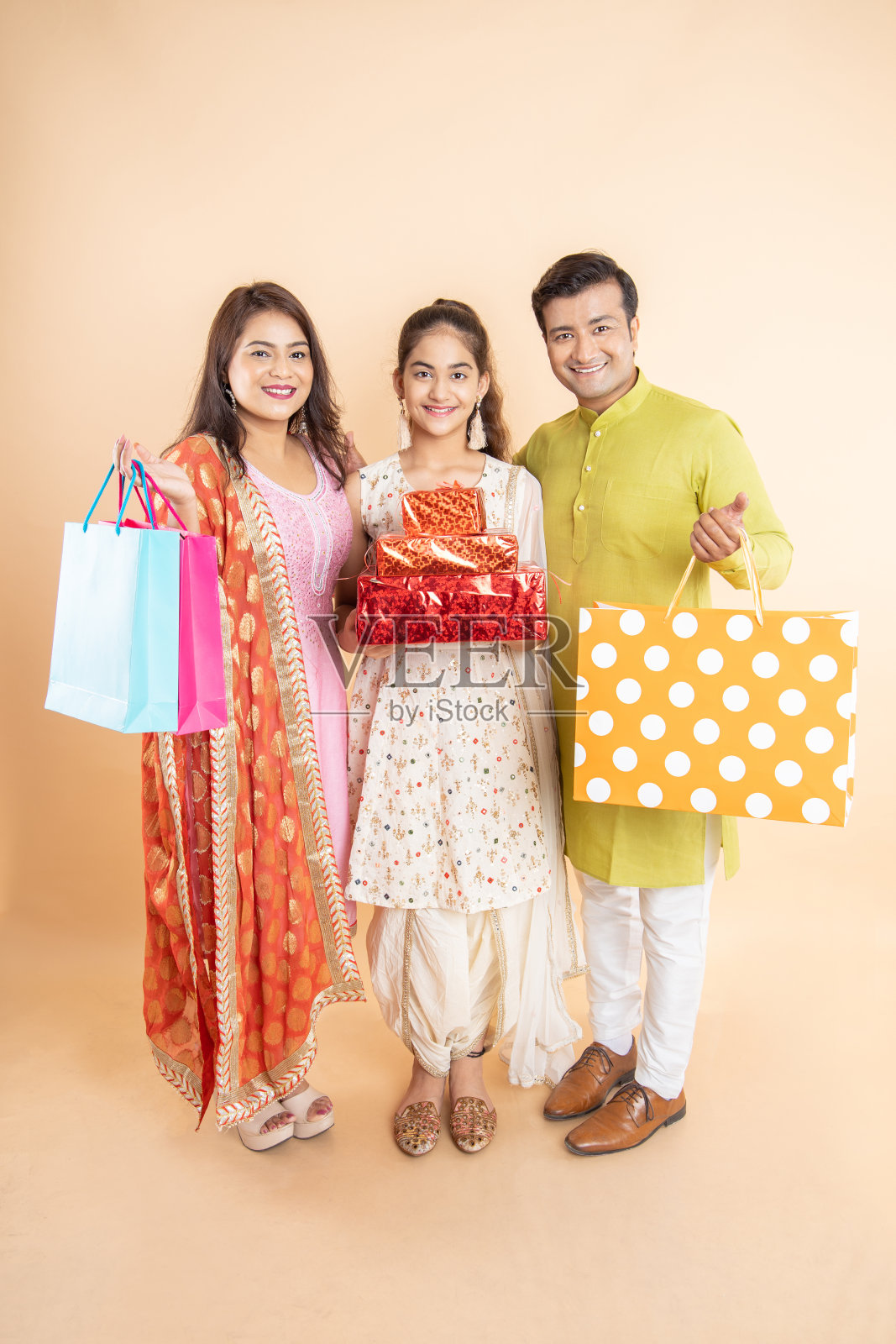 快乐的年轻印度家庭拿着礼盒和购物袋一起庆祝排灯节孤立的工作室背景。节日购物大甩卖，看着相机。照片摄影图片
