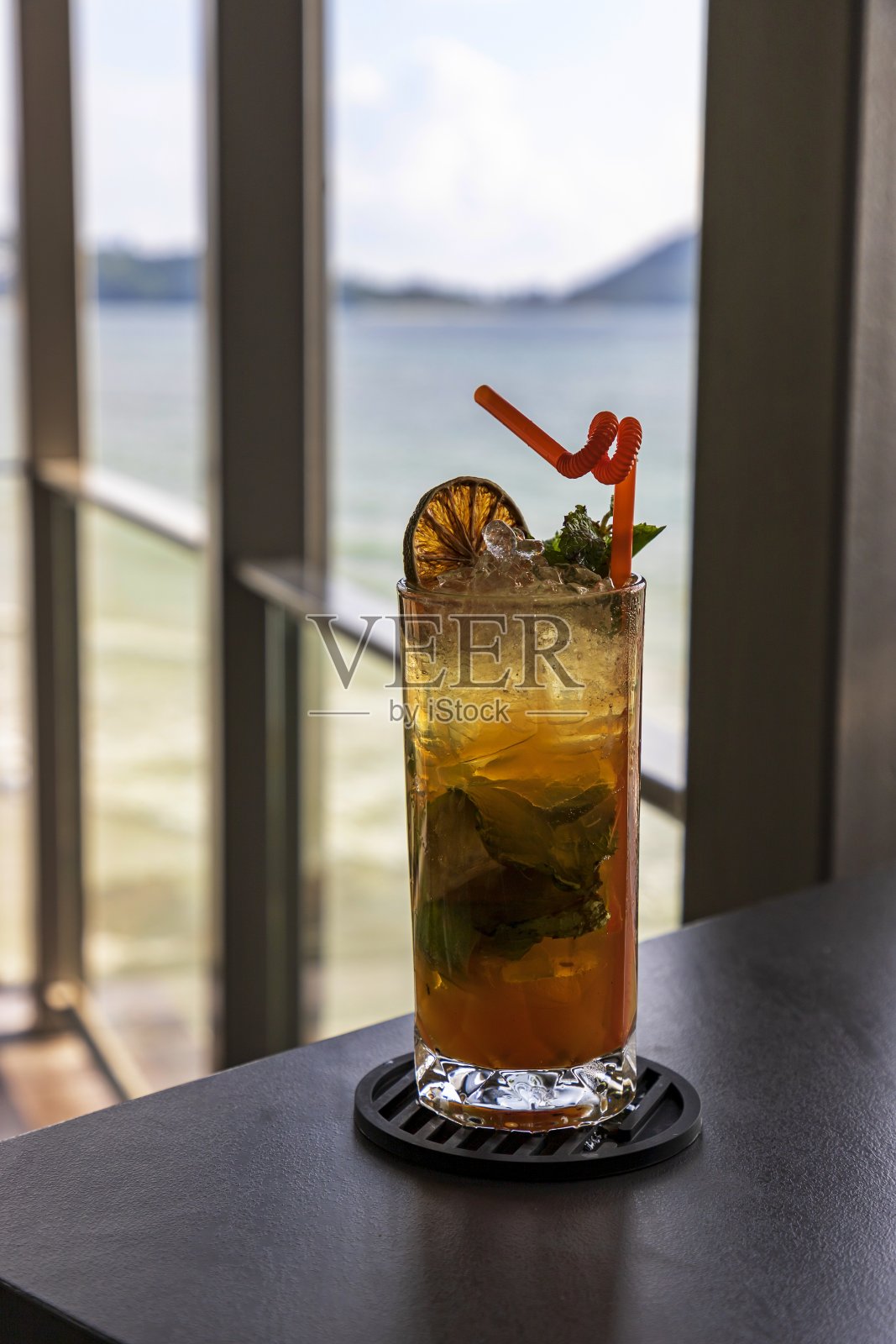 在一家靠海的餐厅里，在木阳台上的桌子上放着一杯甜而清新的水。白天，山和蓝天是多云的。有选择性的重点照片摄影图片