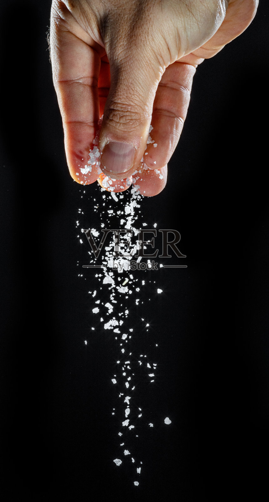 男性的手撒食用盐在黑色背景。照片摄影图片