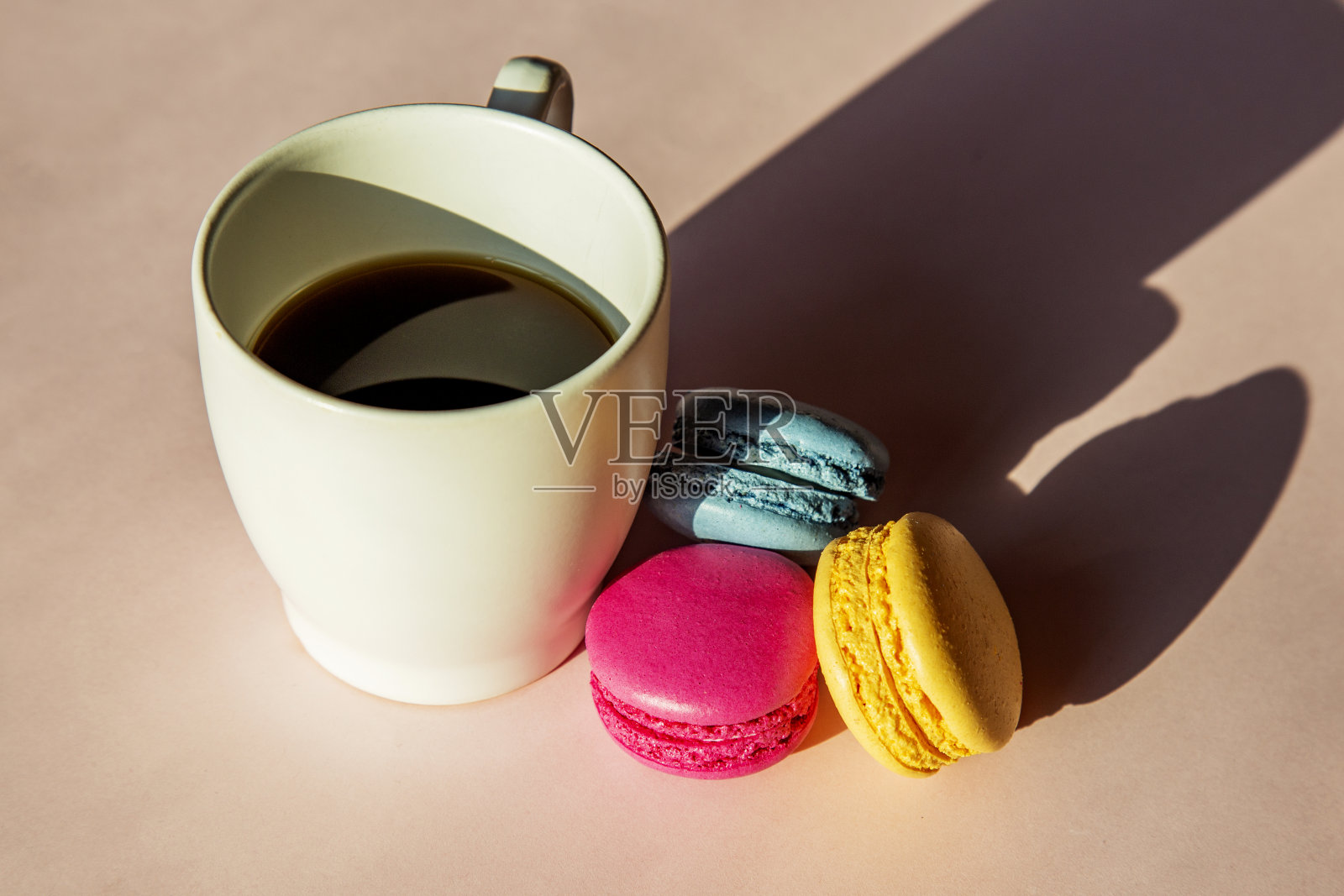 粉红色、黄色和蓝色的彩色马卡龙和一杯粉红色背景的咖啡照片摄影图片