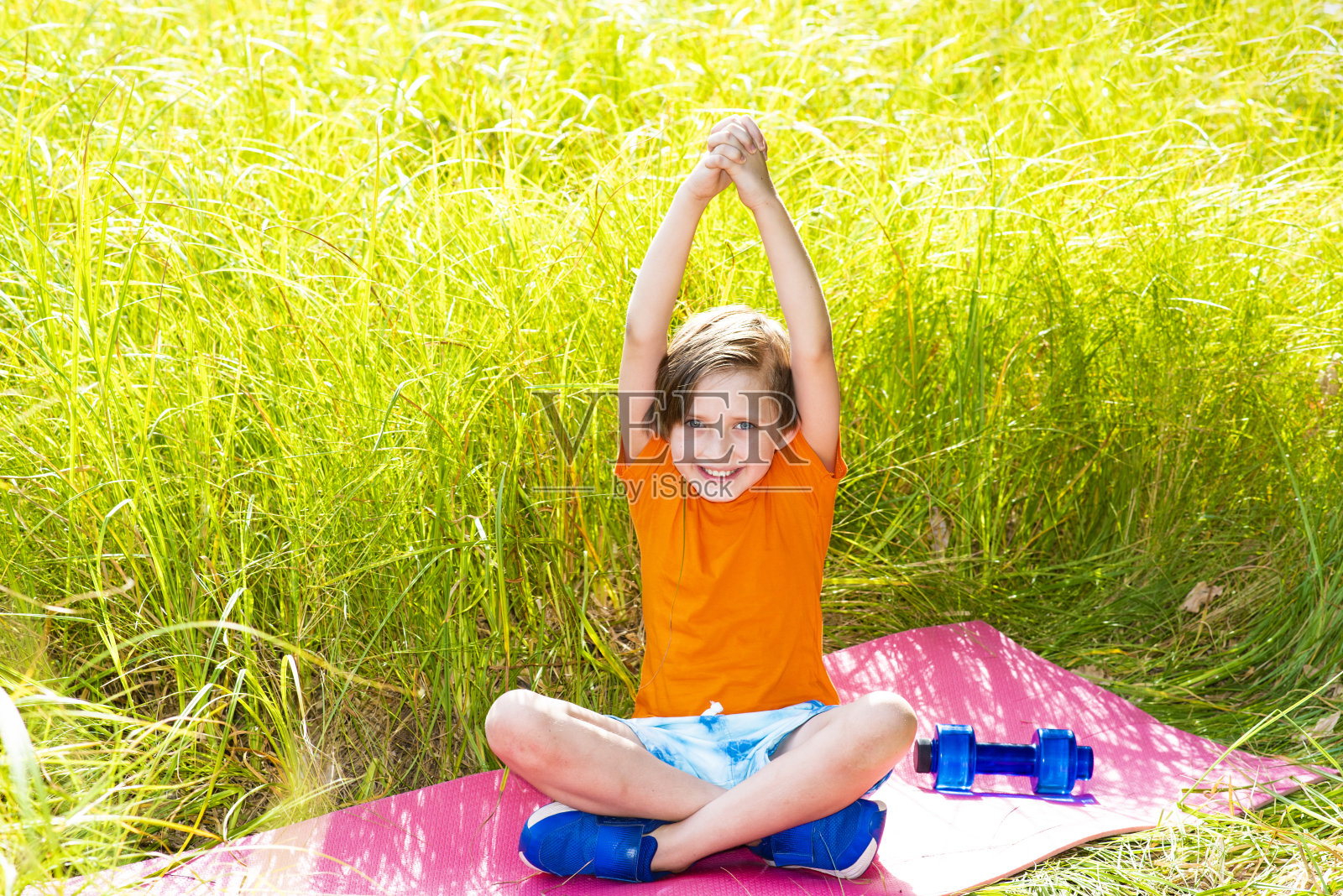 一个小男孩正在室外大自然的垫子或地毯上从事健身、瑜伽、锻炼照片摄影图片