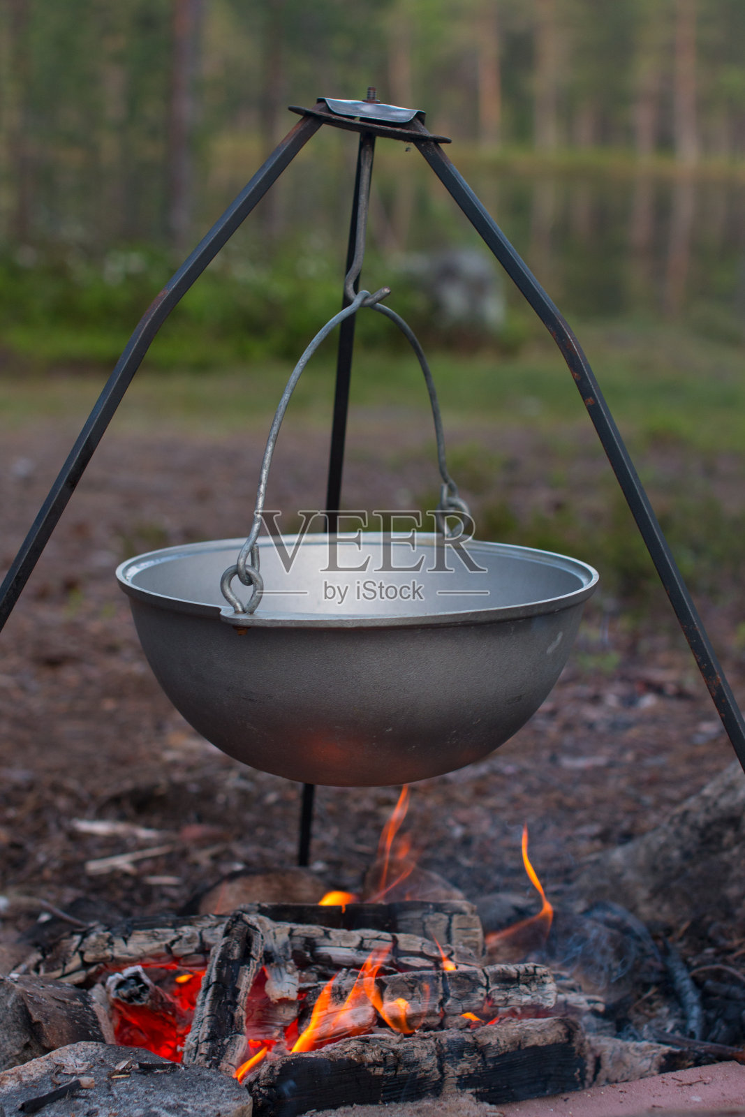 一个露营锅挂在三脚架上。在露营旅行中做饭，徒步旅行照片摄影图片