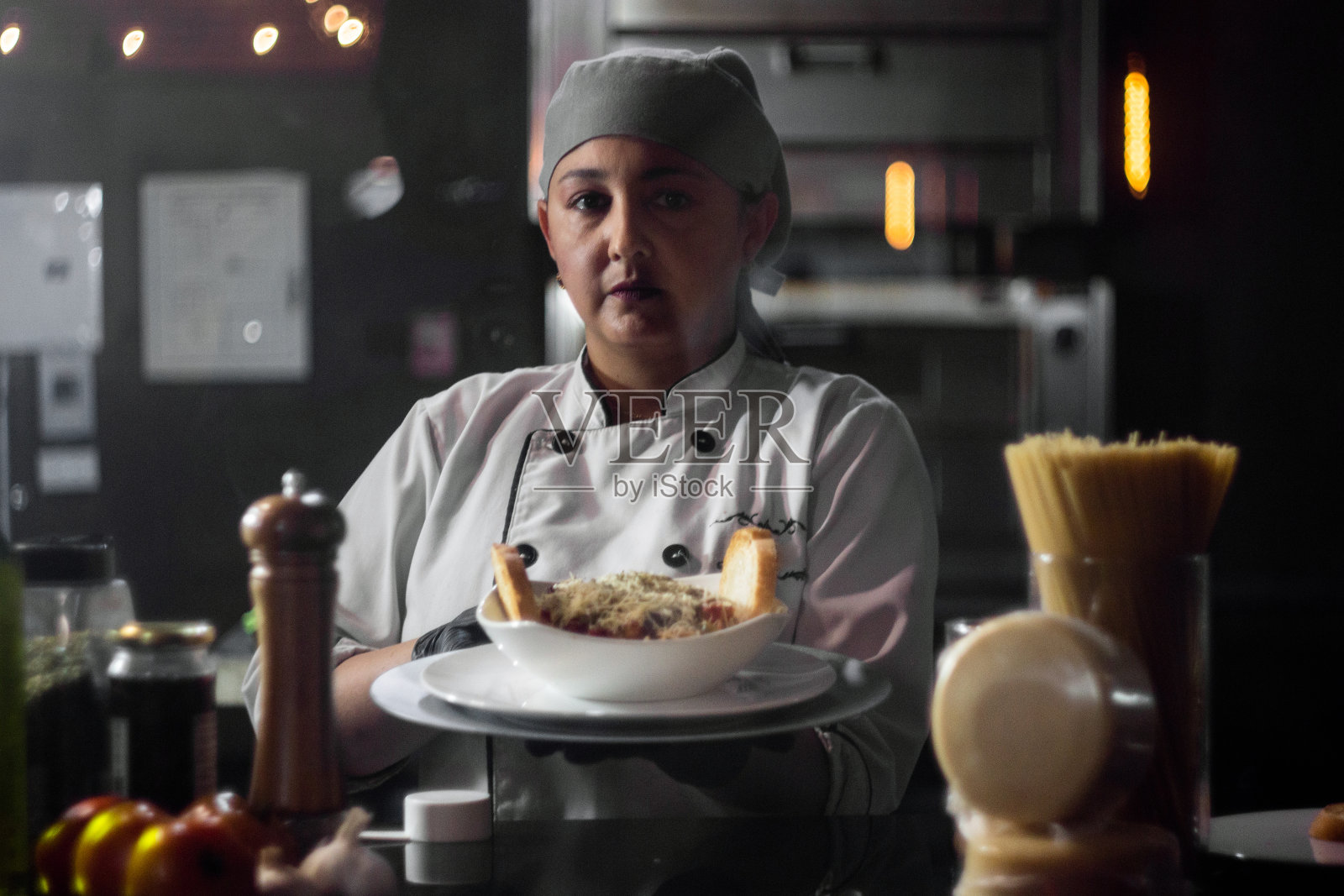 女人想要一份深色背景的面包意大利面和白色意大利辣酱。强大的厨房。站在炉子旁边的年轻女子在厨房做饭。照片摄影图片