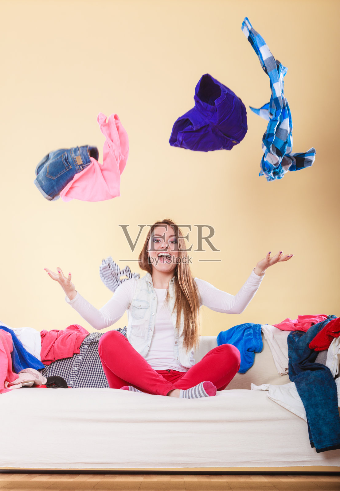 快乐的女人坐在凌乱房间的沙发上扔衣服照片摄影图片