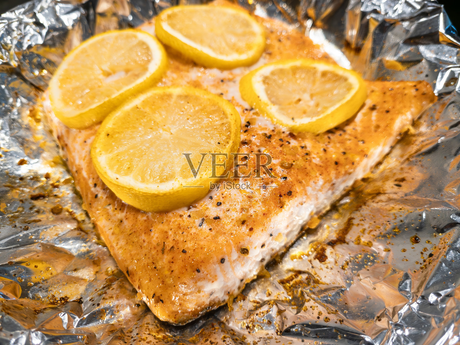 用铝箔盖上柠檬片，煮熟并调味的大西洋鲑鱼。照片摄影图片