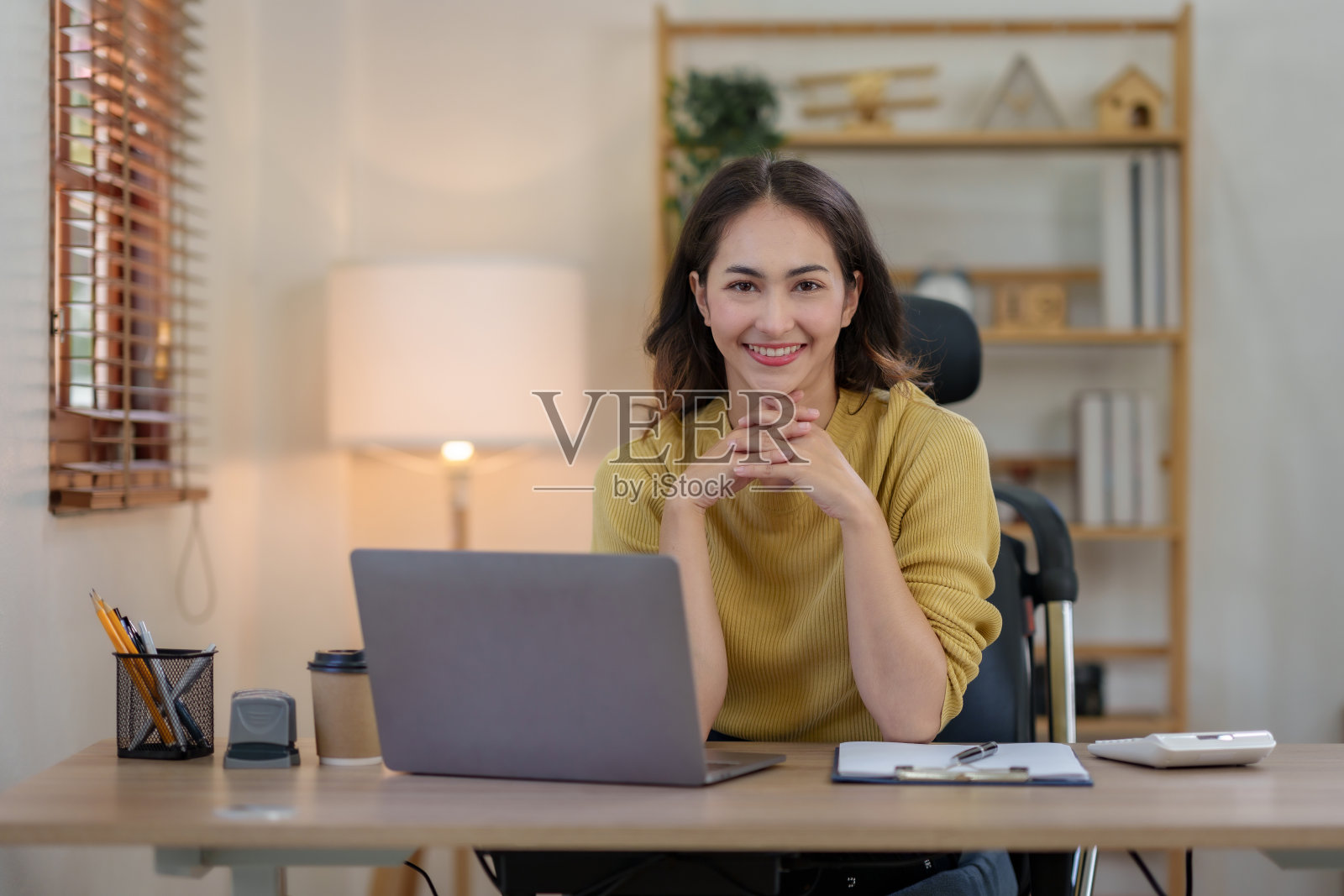 迷人的亚洲女商人使用笔记本电脑在办公室工作，带着灿烂的微笑，看着镜头。照片摄影图片