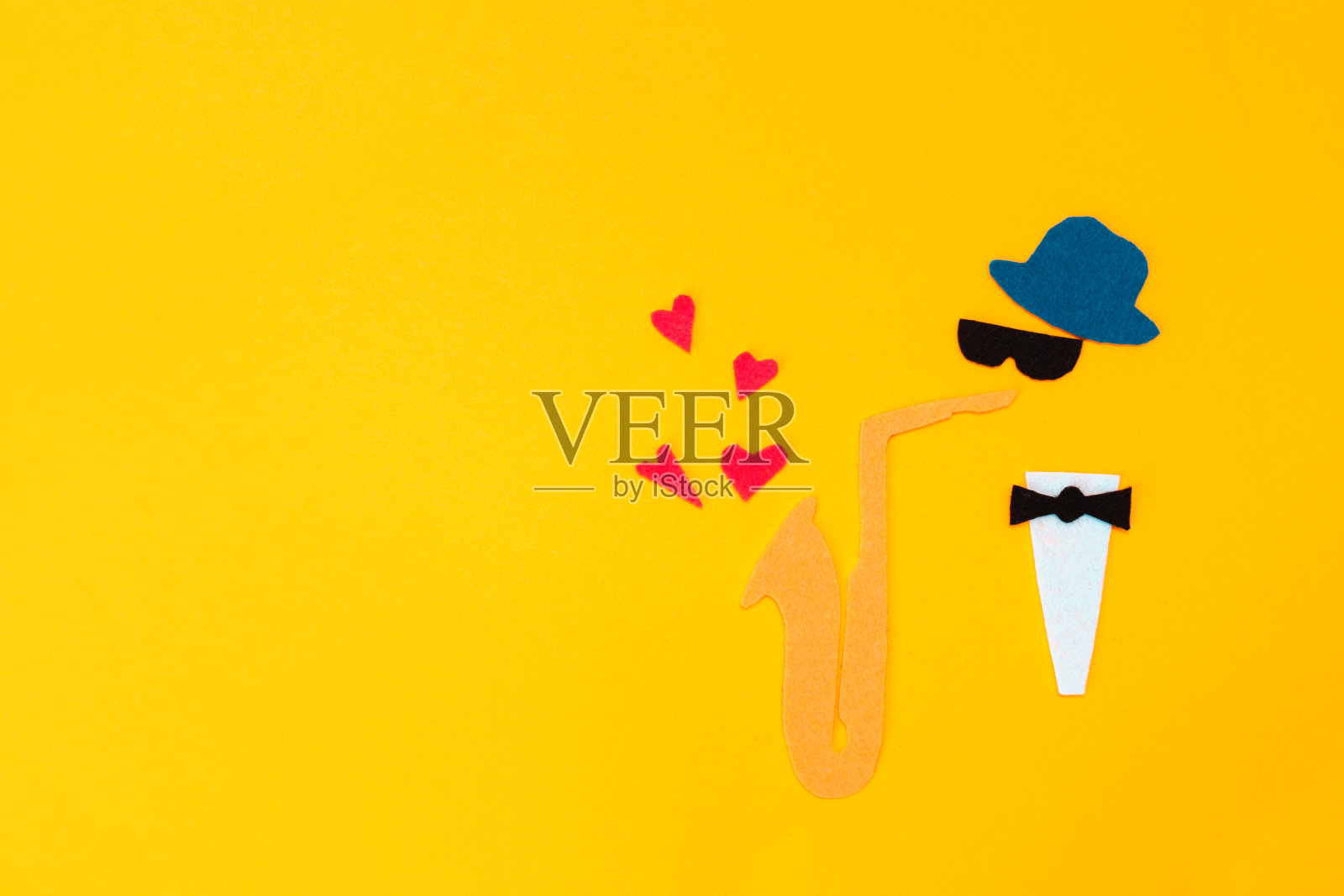 国际爵士乐的一天。一个拿着萨克斯管的音乐家的剪影，黄色背景上的心和飞出来，用毛毡剪成。副本的空间。平躺照片摄影图片