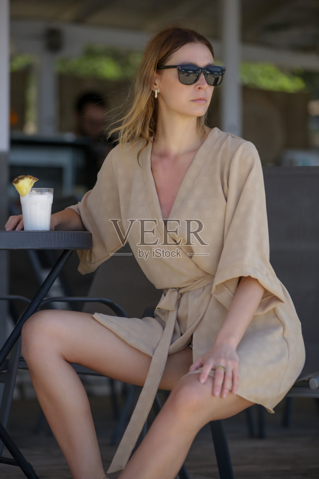 穿着亚麻布长袍的女游客在海滩酒吧喝着鸡尾酒，轻松的独自度假概念照片摄影图片