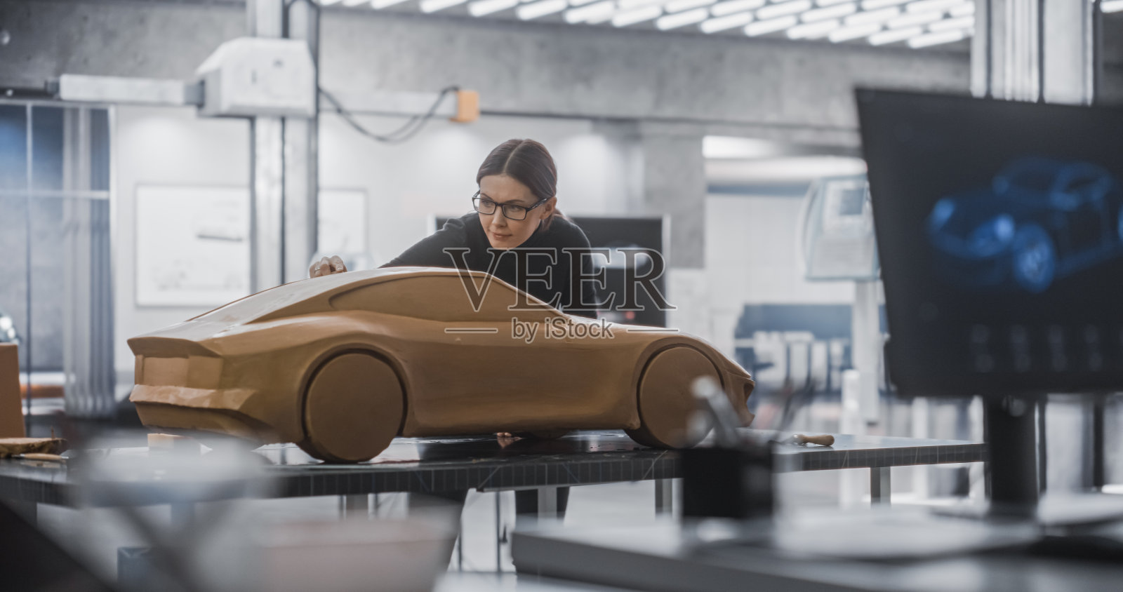 汽车设计师在计算机上使用3D软件。近距离在屏幕上的焦点和女性建模师创建一个粘土模型的汽车。在产品设计机构工作的年轻专家团队照片摄影图片