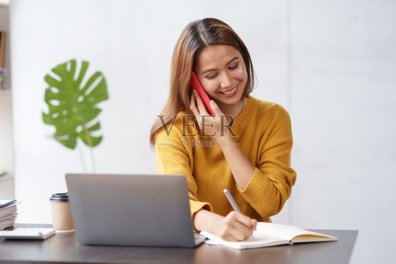 美丽的亚洲商务女性在电话上与客户聊天，在她的笔记本电脑上工作，并在办公室热情愉快地做笔记。照片摄影图片