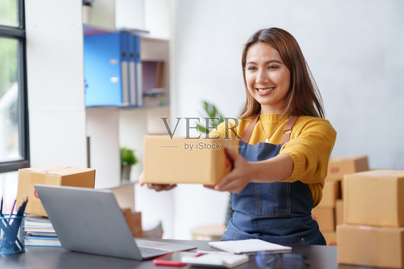 微笑着的亚洲在线企业老板在他的笔记本电脑上准备包裹和检查在线订单，以便交付给客户。网上销售概念。照片摄影图片