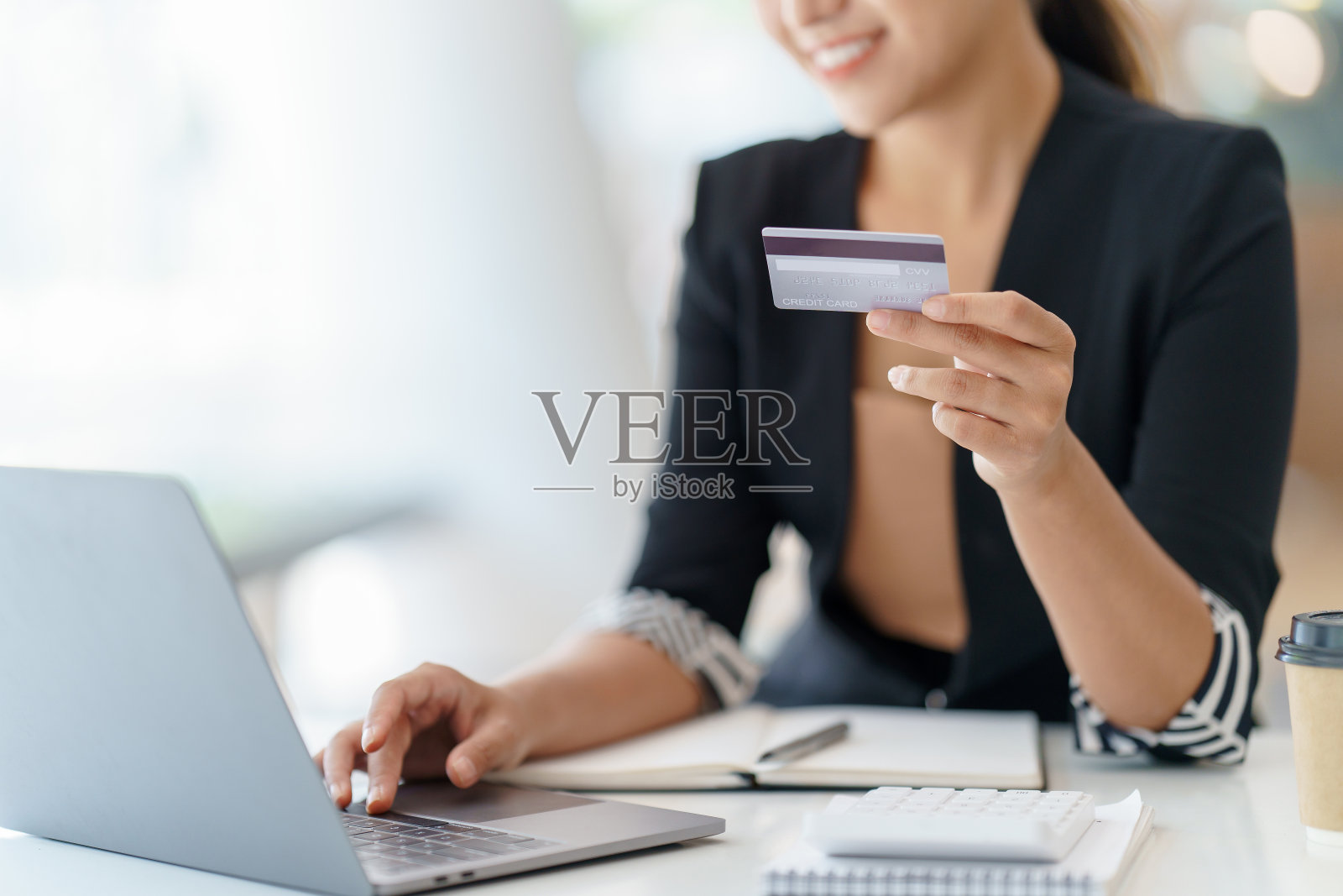 特写的女人享受网上购物与信用卡支付。在办公室用笔记本电脑用信用卡付款。照片摄影图片