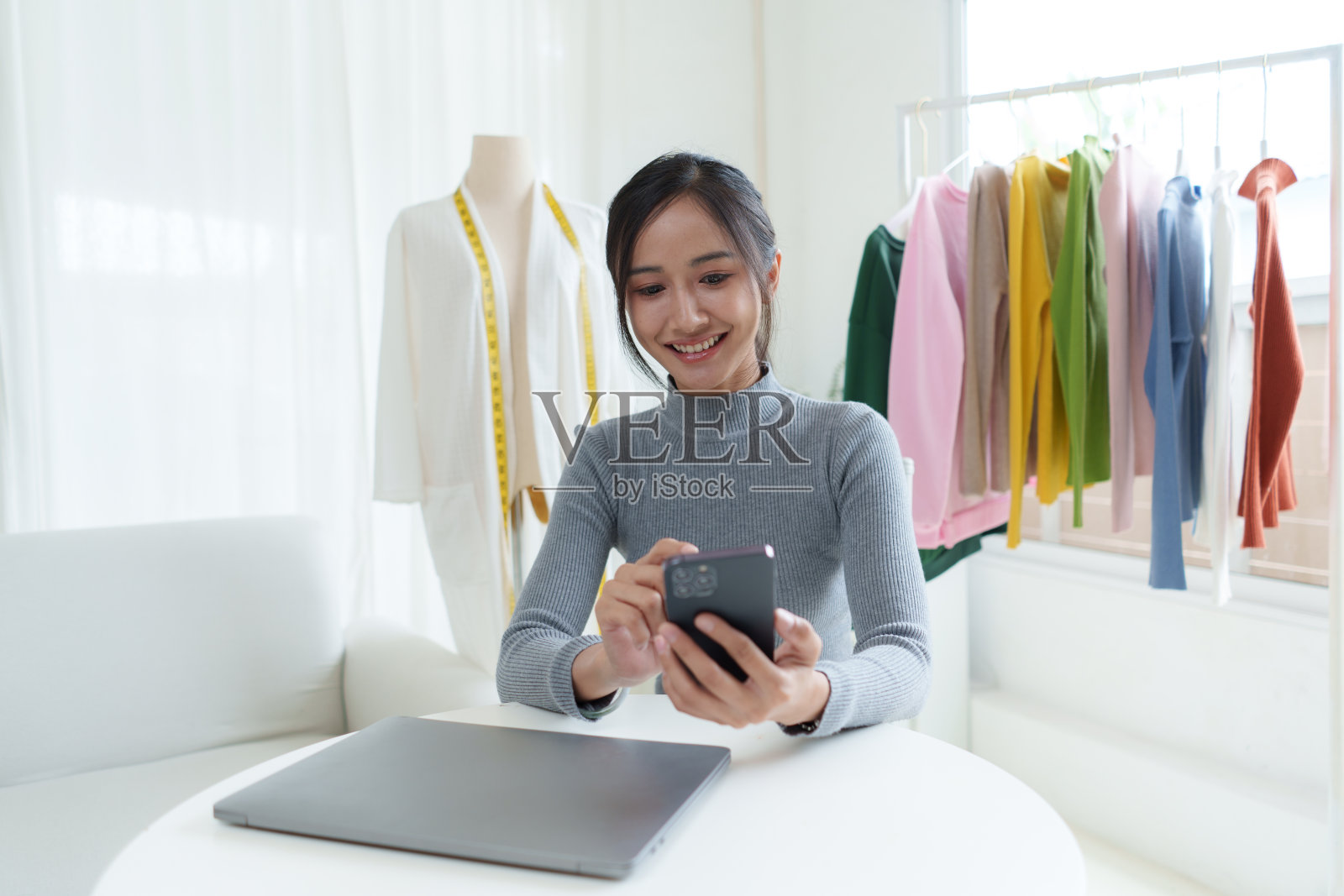 美丽的亚洲女性时装设计师坐在服装商店和工作室。在摄像机前录制视频博客直播。社交媒体概念上的商业在线影响者。照片摄影图片