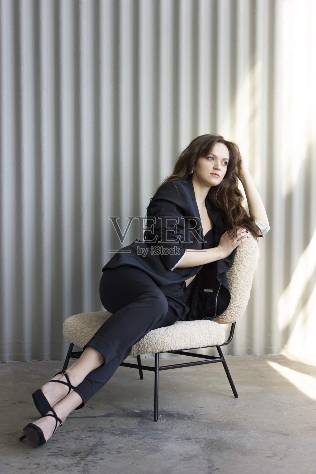 漂亮的欧洲商人，棕色长发，穿着西装，坐在椅子上，想着什么，白色的背景。垂直平面。摄影工作室照片摄影图片