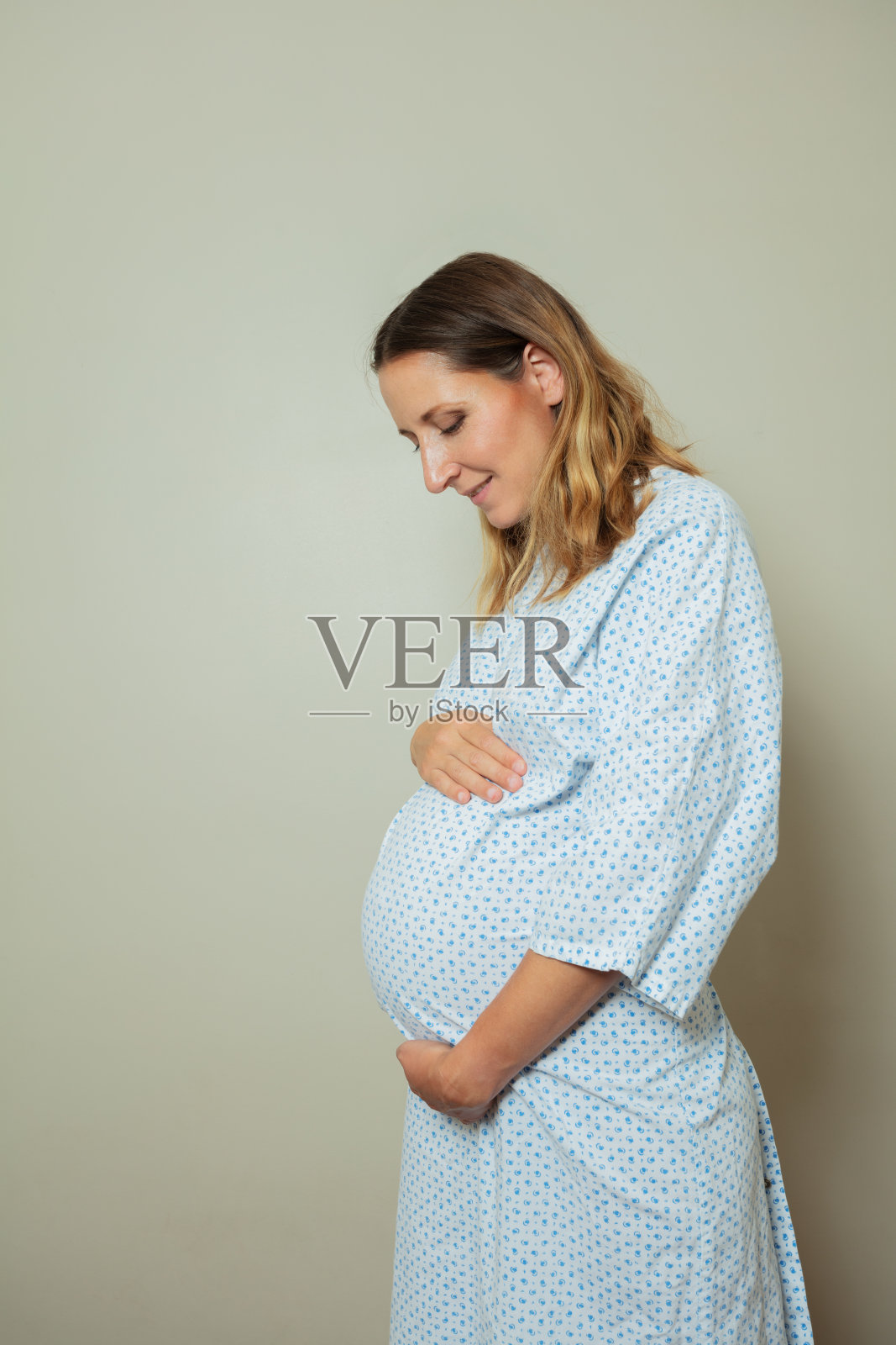 身穿医院病号服，手捧大肚子侧面像的孕妇照片摄影图片