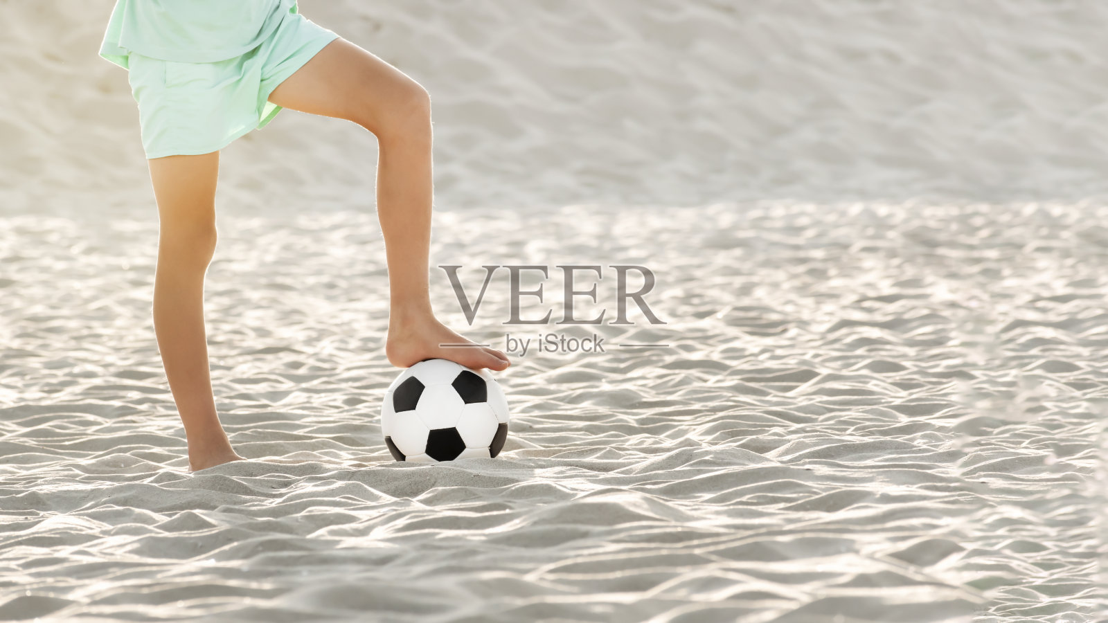 沙滩足球。足球运动员男孩光着脚和球在沙滩上。儿童暑期体育游戏和活动照片摄影图片