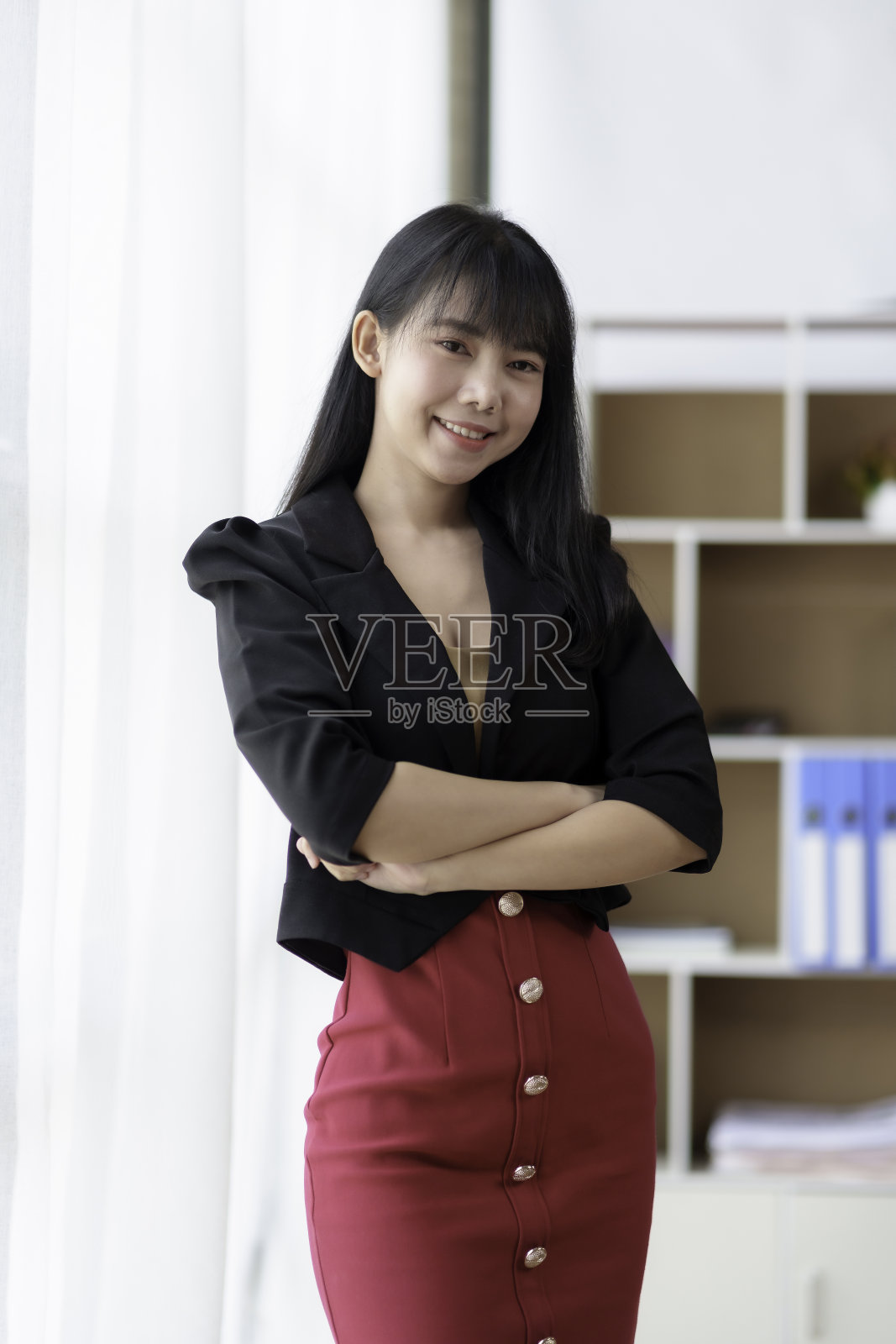 美丽的亚洲女商人站在她的双臂交叉，自信地看着镜头在办公室。照片摄影图片