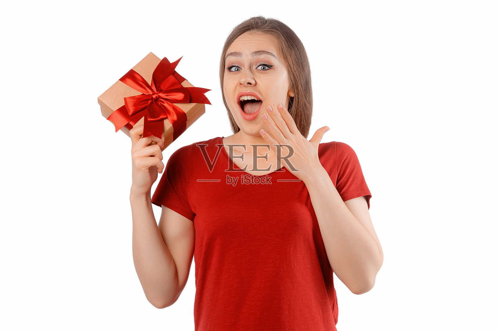 一个穿着红色t恤的快乐微笑的女孩的肖像，拿着礼物盒，在白色背景上摆姿势。开朗的黑发女人长着头发，微笑着，笑着，看起来很高兴照片摄影图片