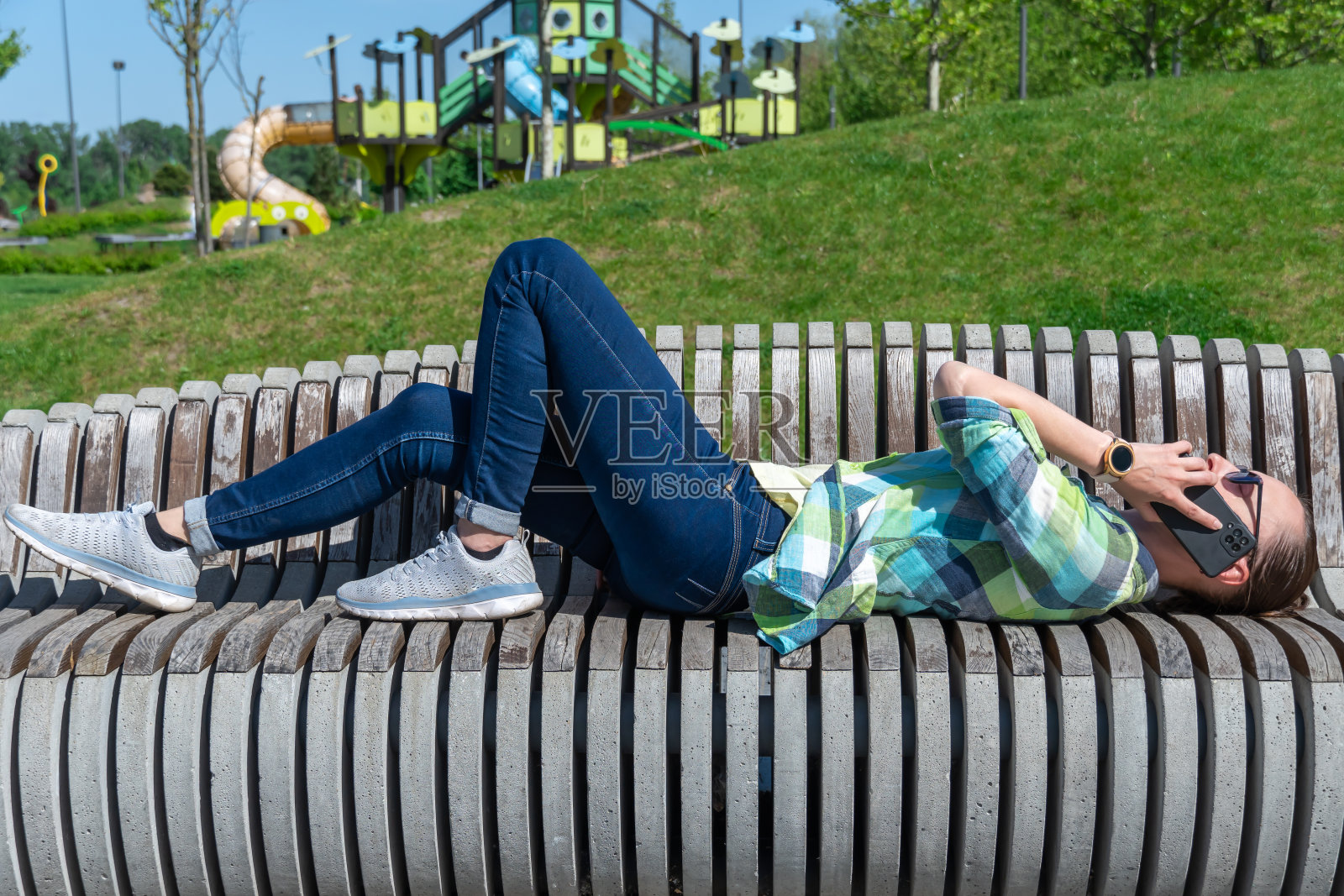 一个女人躺在公园的长椅上打电话。照片摄影图片