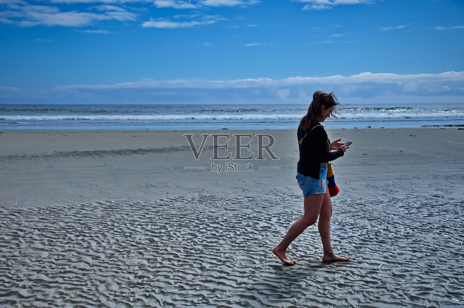 一个女人走在沙滩上玩手机照片摄影图片