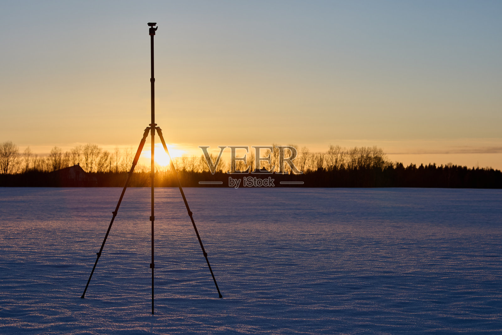 摄影器材，摄影三脚架，在冬天的雪地上，在日落的时候站在野外。照片摄影图片