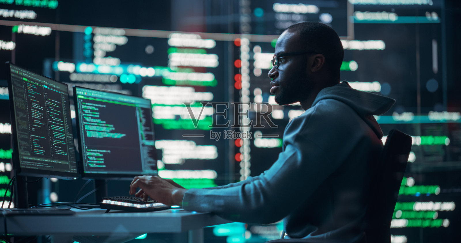 一名黑人男性程序员在监控室工作，周围是显示编程语言代码的大屏幕。一个人的肖像创造一个软件和编码照片摄影图片