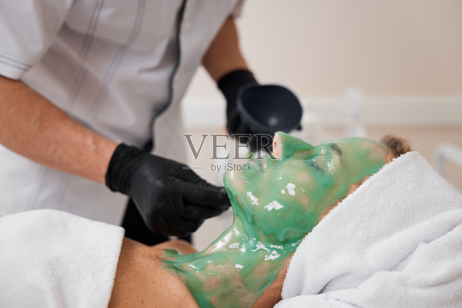 美容师将海藻酸盐面膜涂在女士的脸上照片摄影图片