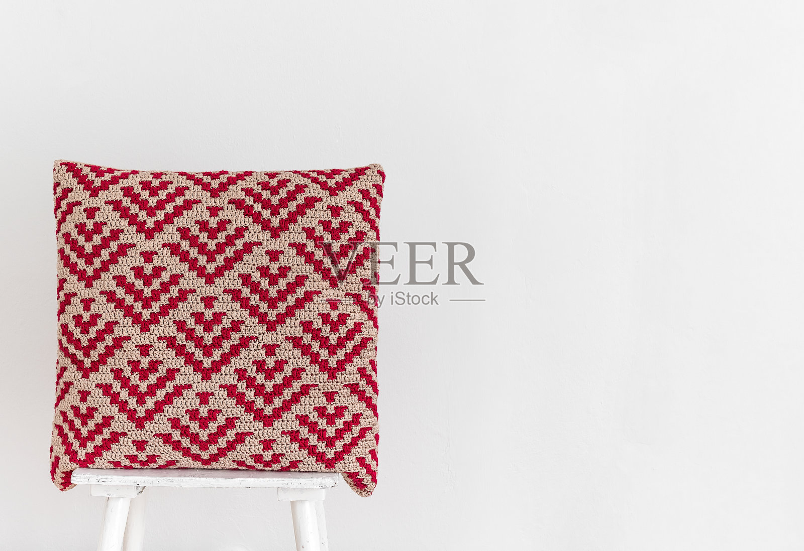 手工红色钩针枕头与抽象马赛克图案的椅子对着白色的墙壁。副本的空间。照片摄影图片