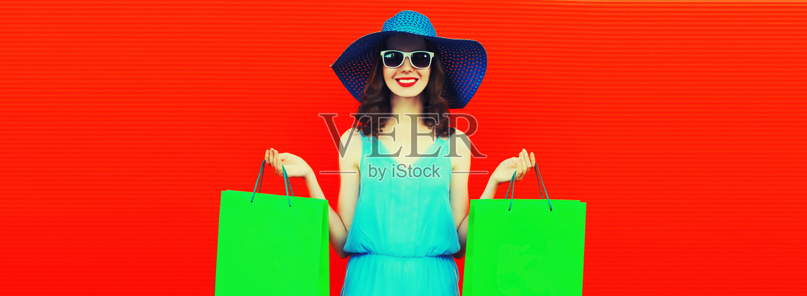 美丽的幸福微笑的年轻女子的肖像与五颜六色的购物袋戴夏天的草帽在橙色的背景，空白的拷贝空间的广告文字照片摄影图片