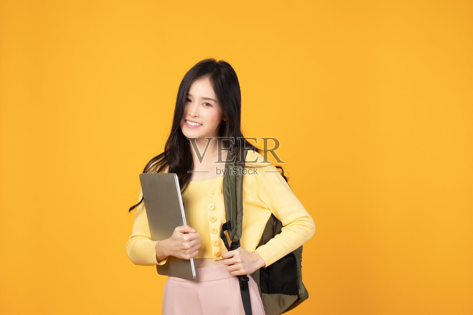 肖像快乐休闲的亚洲女学生与背包和笔记本电脑孤立的黄色背景。回归学校和学习理念。照片摄影图片