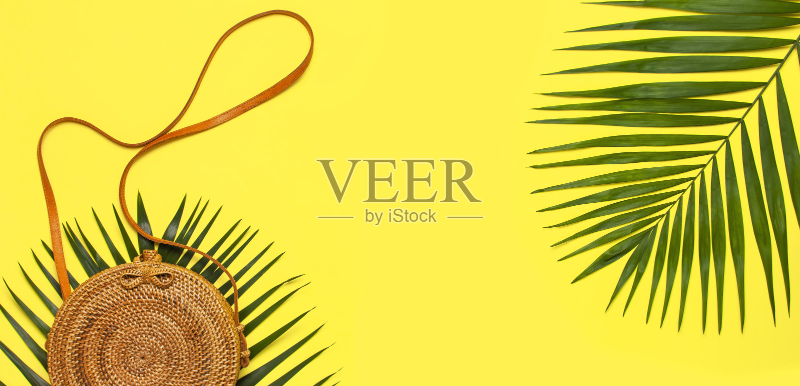 夏季时装平铺。时尚手工自然圆藤袋和热带棕榈叶在黄色的背景。俯视图拷贝空间。来自巴厘岛的时尚竹袋Ecobags。热带的背景照片摄影图片