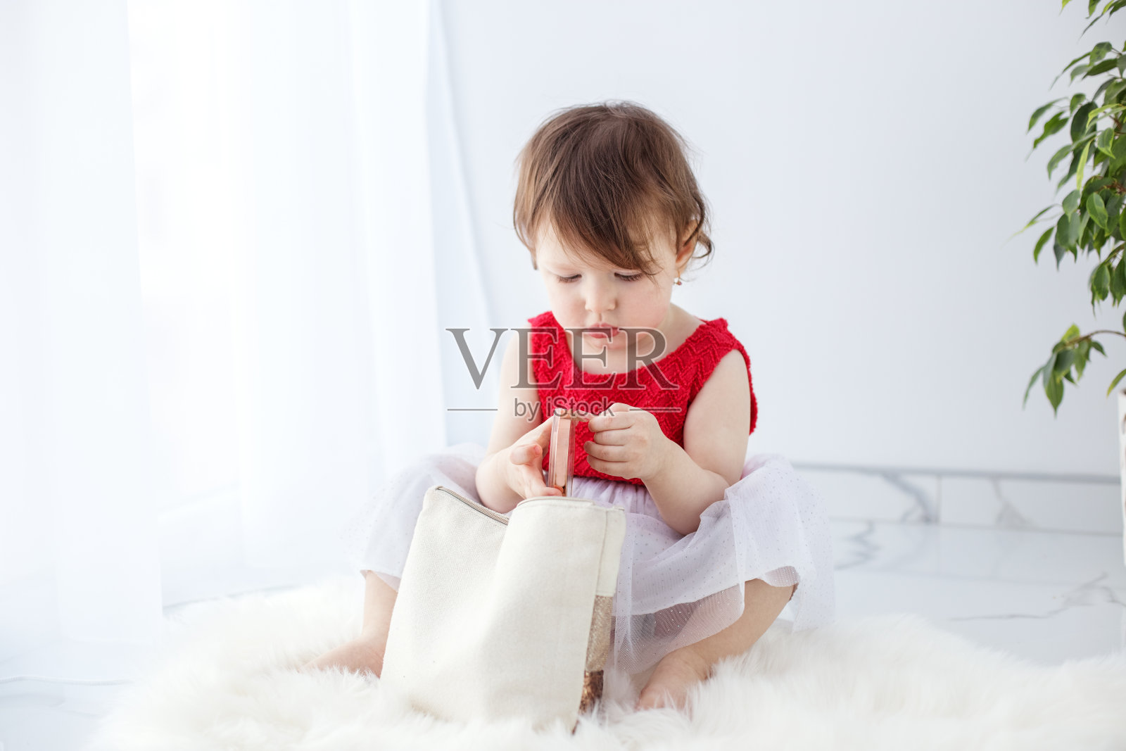 一个穿着红色外套的女孩发现了妈妈的化妆包，手里拿着化妆品学习化妆照片摄影图片